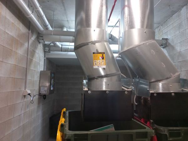 Two garbage chutes discharging into bins, with a Garbage Doctor unit on the wall beside them